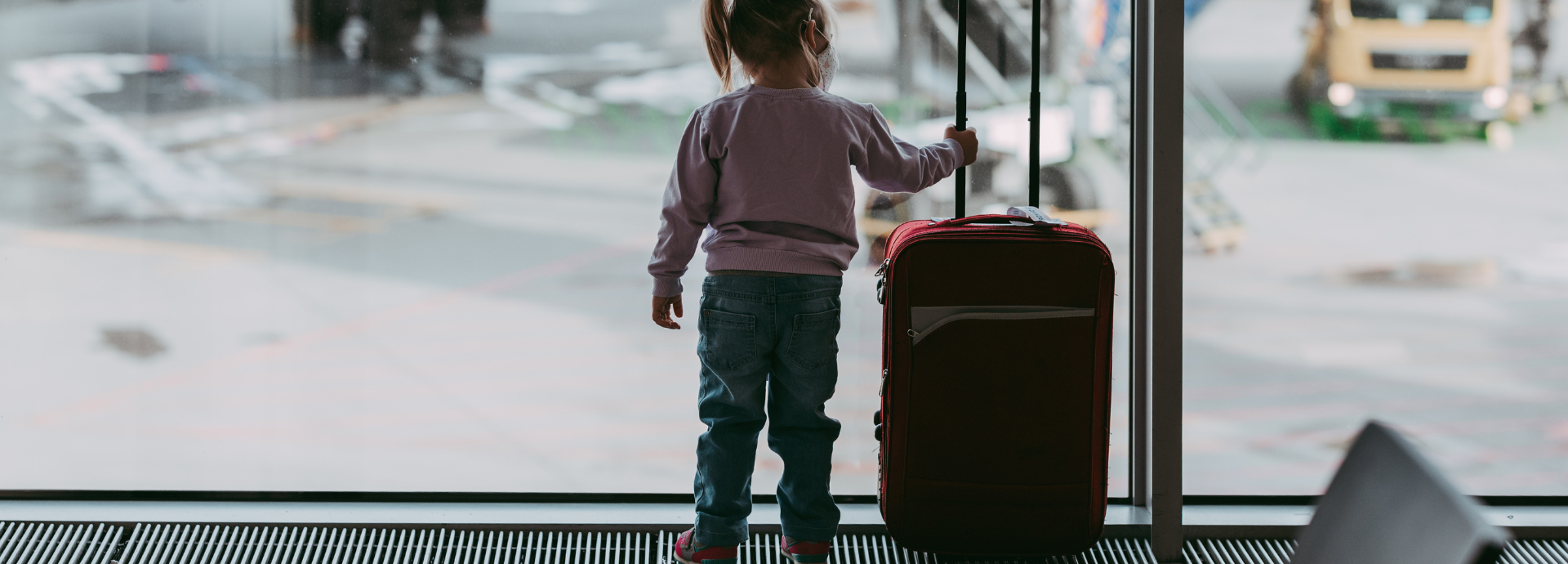 child at airport with suitcase looking at the planes