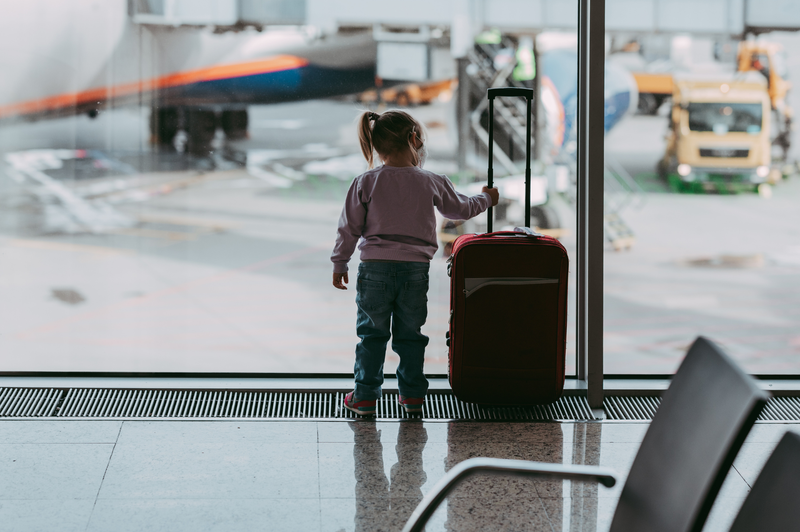 child at airport with suitcase looking at the planes